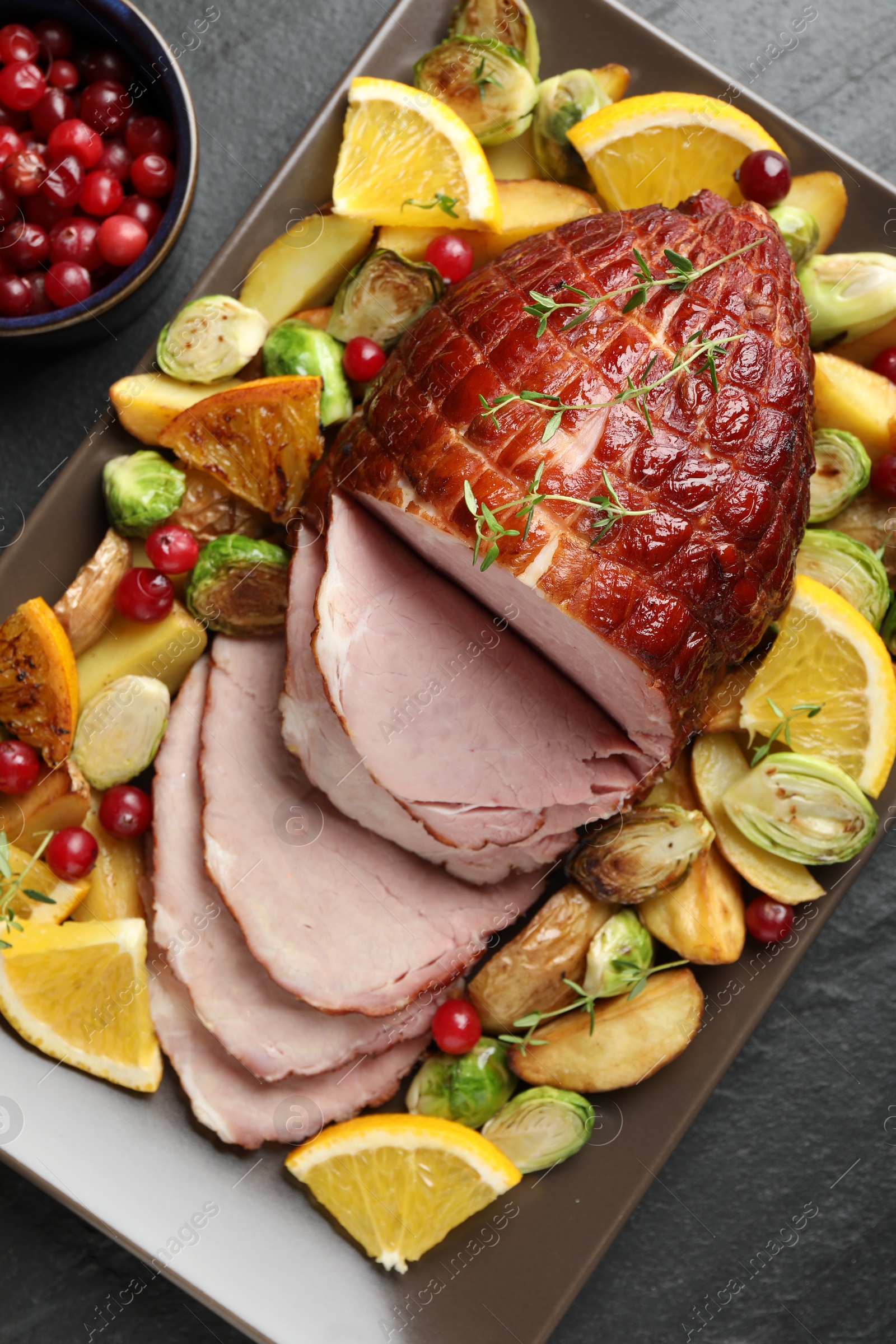 Photo of Tasty baked ham served with vegetables and oranges on black table, top view