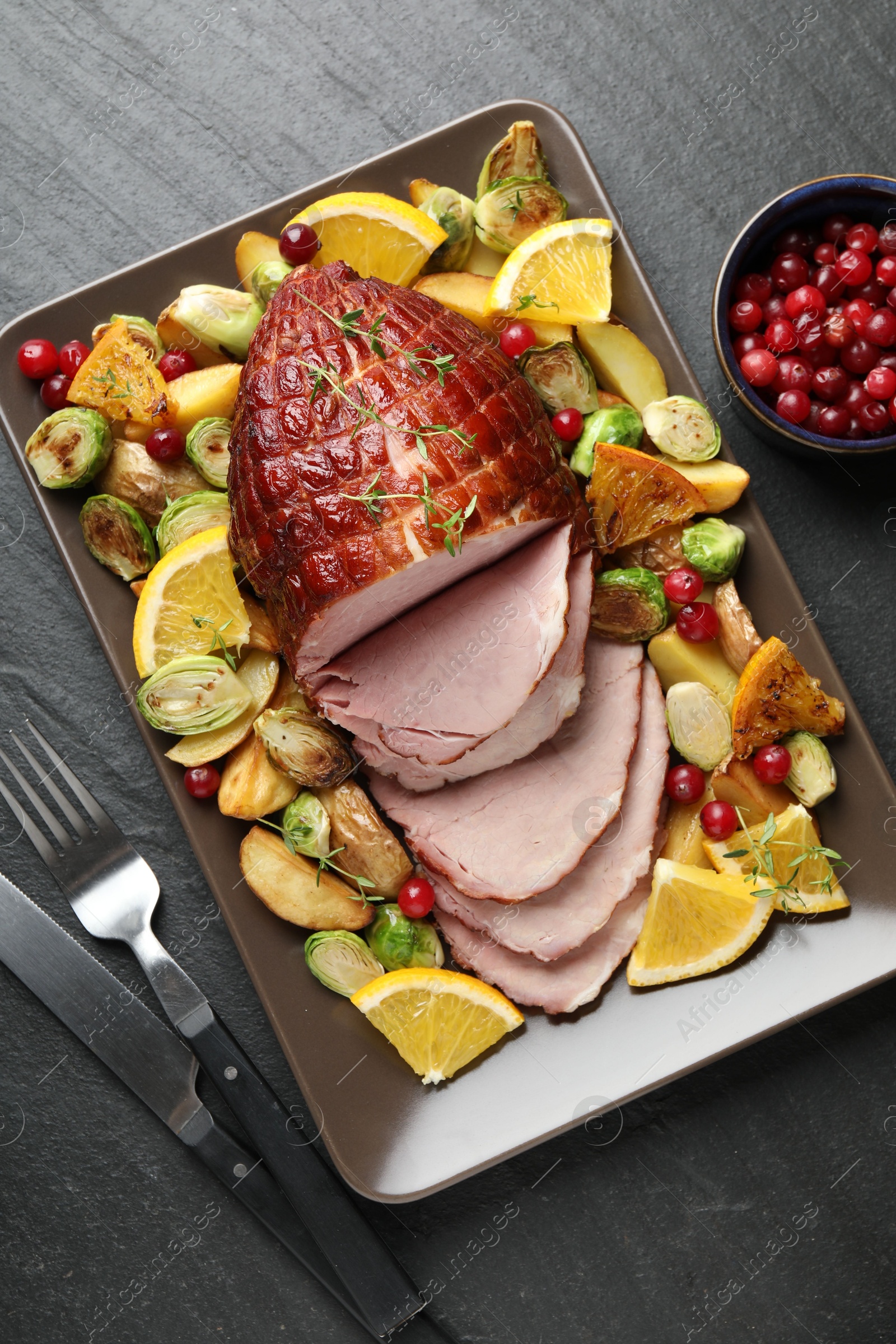 Photo of Tasty baked ham served with vegetables and oranges on black table, flat lay