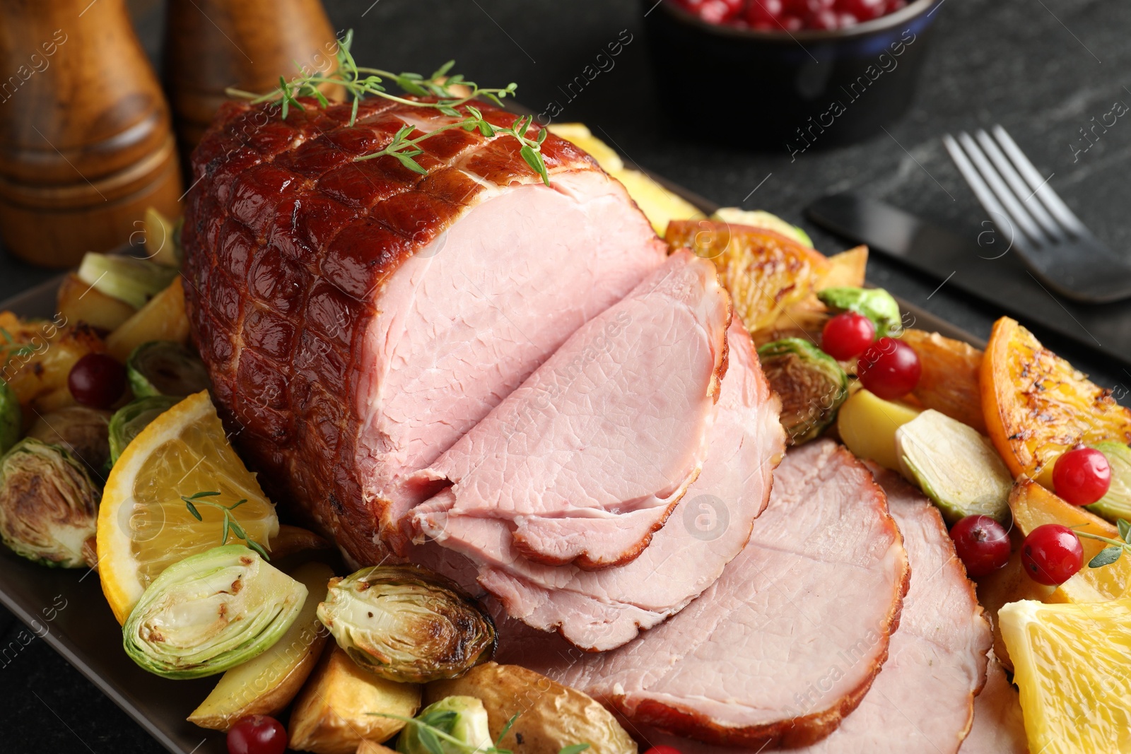 Photo of Tasty baked ham served with vegetables and oranges on black table, closeup