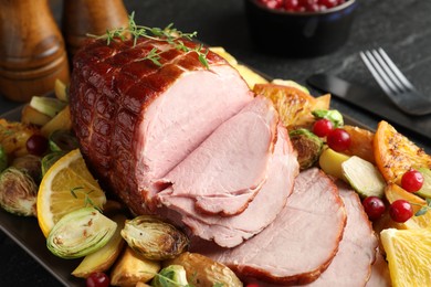 Tasty baked ham served with vegetables and oranges on black table, closeup