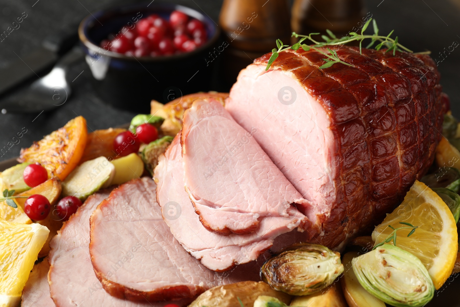 Photo of Tasty baked ham served with vegetables and oranges on black table, closeup