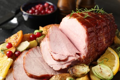 Tasty baked ham served with vegetables and oranges on black table, closeup