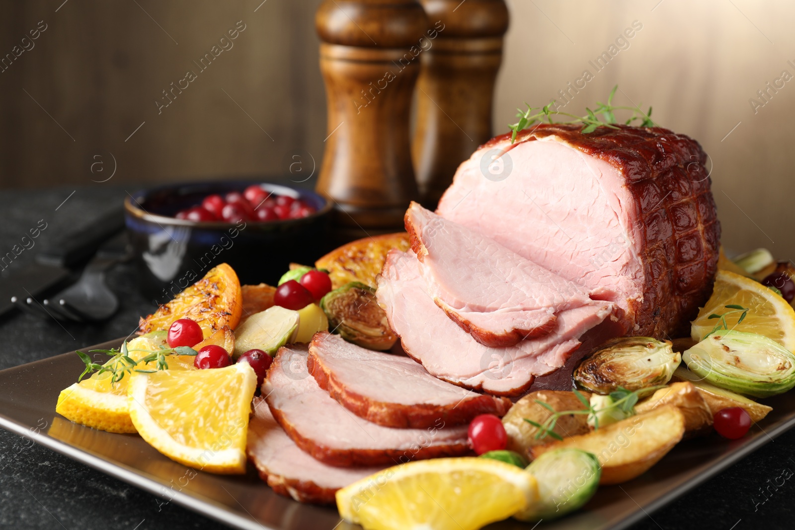 Photo of Tasty baked ham served with vegetables and oranges on black table, closeup