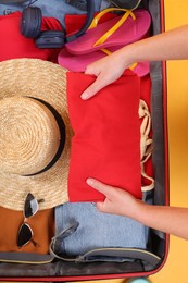 Traveler packing suitcase on yellow background, top view