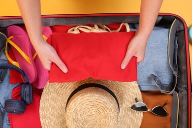 Traveler packing suitcase on yellow background, top view