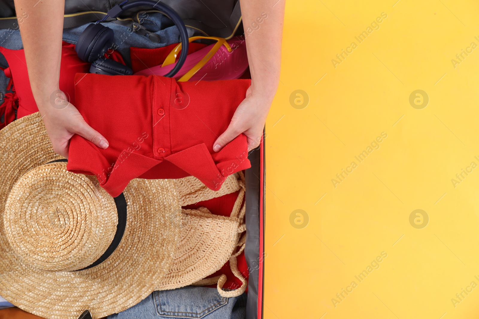 Photo of Traveler packing suitcase on yellow background, top view. Space for text