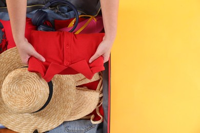 Photo of Traveler packing suitcase on yellow background, top view. Space for text