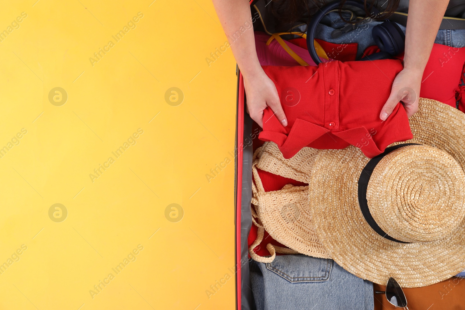 Photo of Traveler packing suitcase on yellow background, top view. Space for text