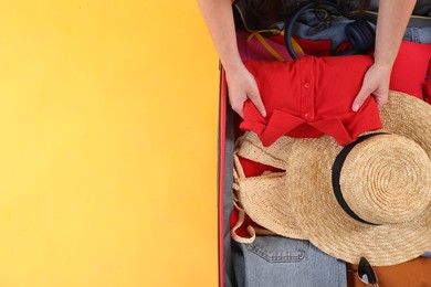 Photo of Traveler packing suitcase on yellow background, top view. Space for text