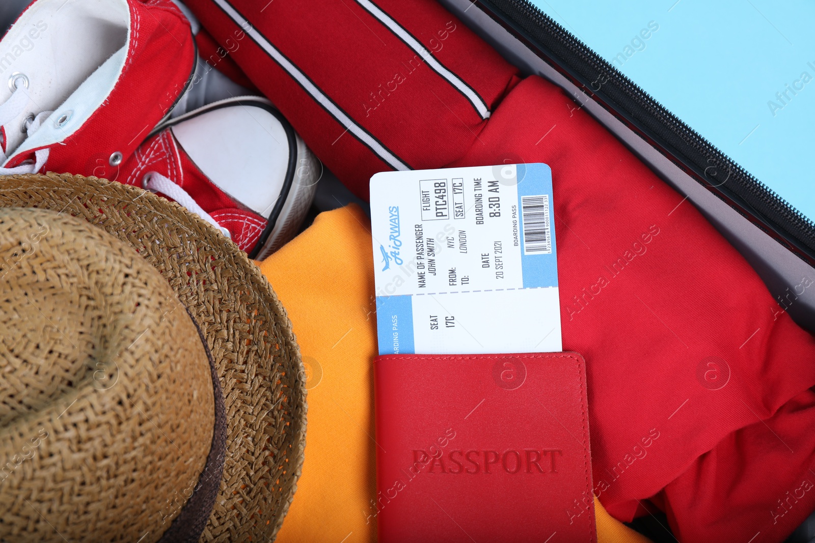 Photo of Travel abroad. Packed suitcase with passport and ticket on light blue background, closeup