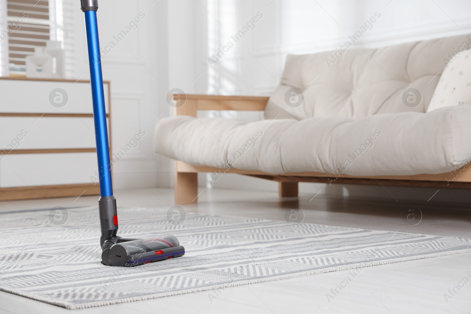 Photo of Cleaning carpet with cordless vacuum cleaner indoors, closeup. Space for text