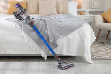 Photo of One cordless vacuum cleaner leaning on bed indoors