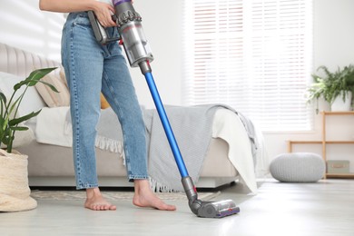 Photo of Woman cleaning floor with cordless vacuum cleaner indoors, closeup