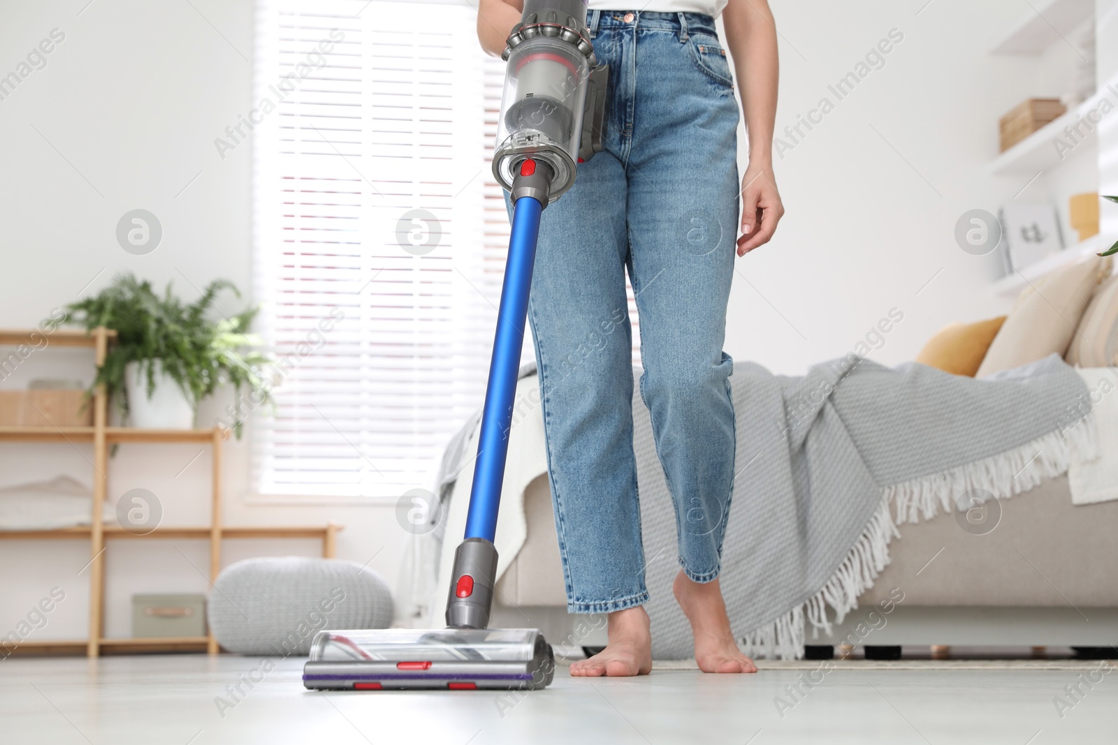 Photo of Woman cleaning floor with cordless vacuum cleaner indoors, closeup