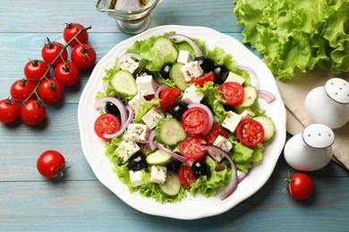 Photo of Delicious salad with feta cheese and ingredients on light blue wooden table, flat lay