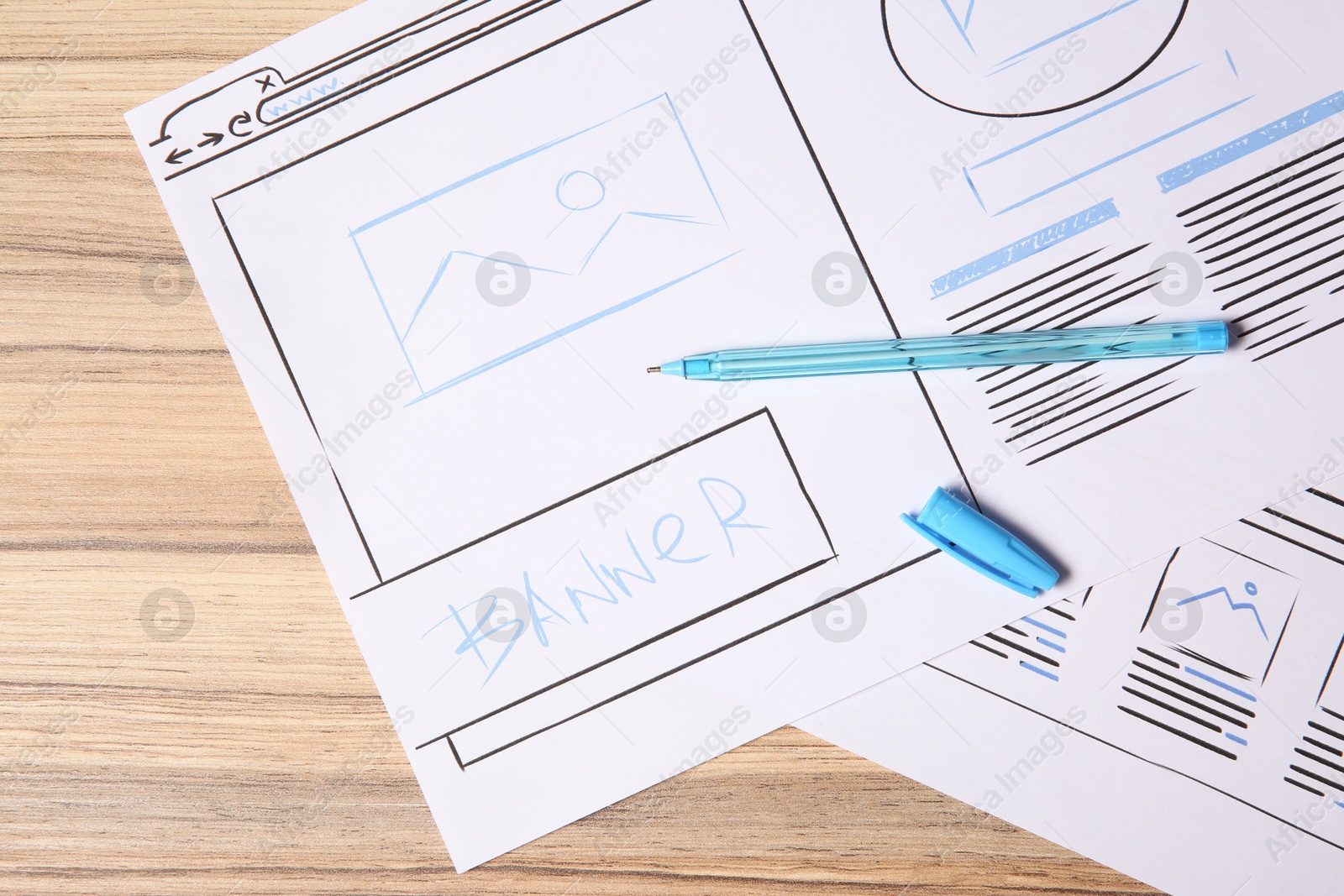 Photo of Website development. Sketches of wireframes and pen on wooden table, flat lay