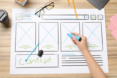 Photo of Website designer creating wireframe on paper with highlighter at wooden table, top view