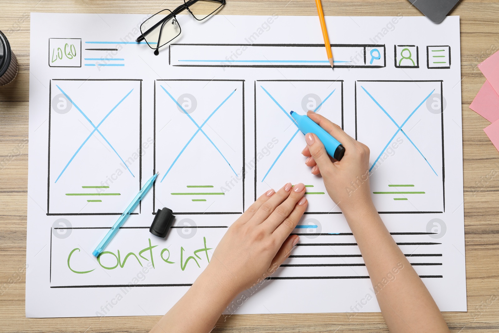 Photo of Website designer creating wireframe on paper with highlighter at wooden table, top view