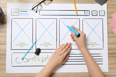 Website designer creating wireframe on paper with highlighter at wooden table, top view