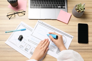 Photo of Website designer creating wireframe on paper with highlighter at wooden table, above view