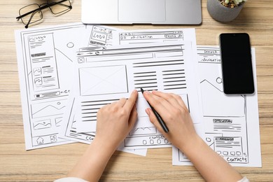 Website designer creating wireframe on paper with pen at wooden table, top view