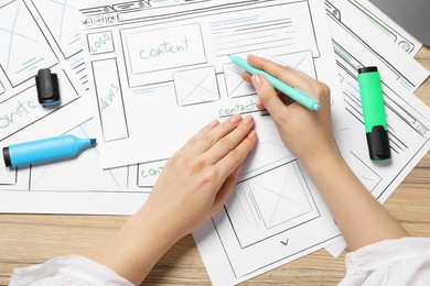 Website designer creating wireframe on paper with pen at wooden table, top view