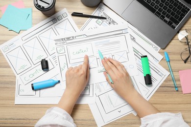 Website designer creating wireframe on paper with pen at wooden table, top view