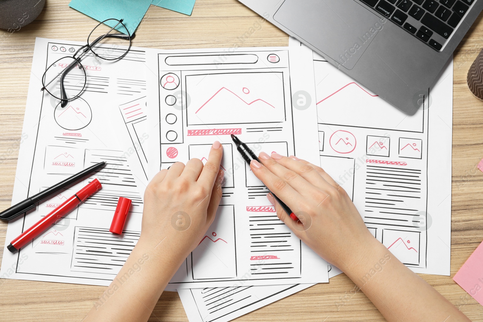 Photo of Website designer creating wireframe on paper with felt pen at wooden table, top view