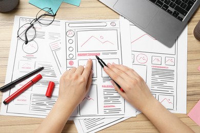 Website designer creating wireframe on paper with felt pen at wooden table, top view