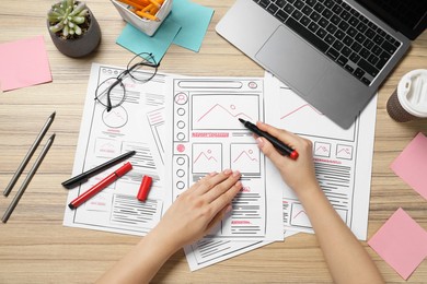 Website designer creating wireframe on paper with felt pen at wooden table, top view