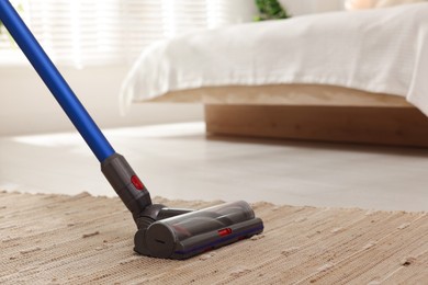 Photo of Cleaning rug with cordless vacuum cleaner indoors, closeup