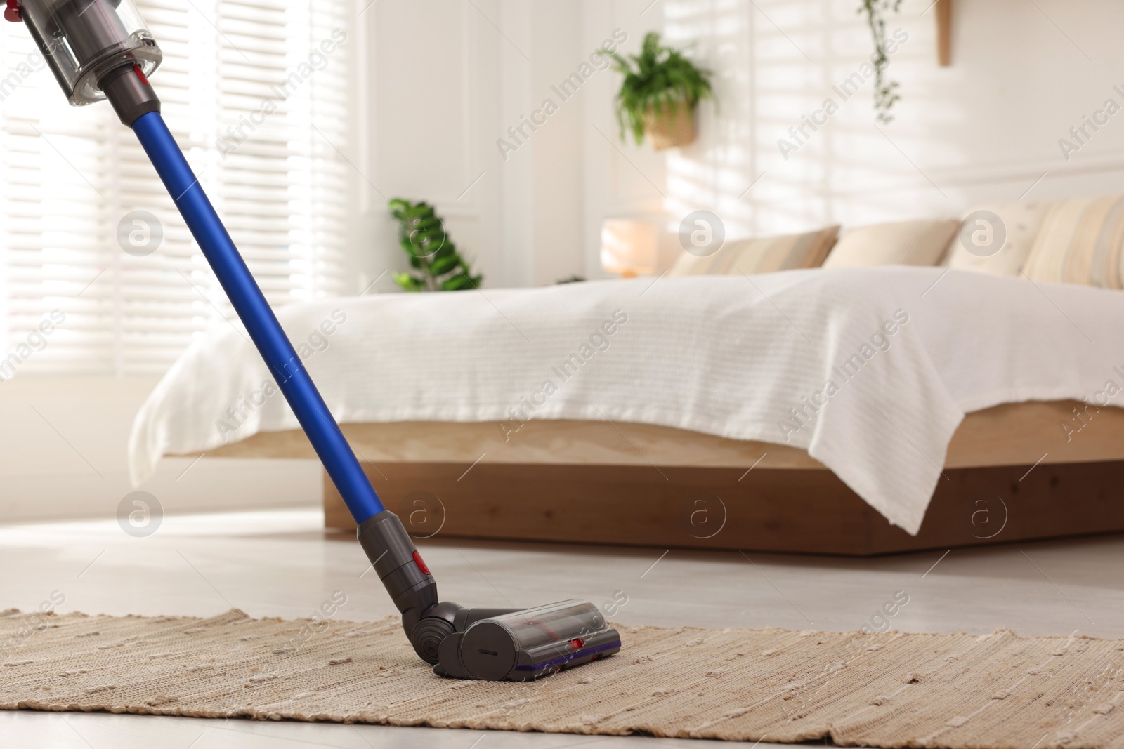 Photo of Cleaning rug with cordless vacuum cleaner in bedroom