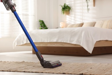 Photo of Cleaning rug with cordless vacuum cleaner in bedroom