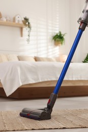 Photo of Cleaning rug with cordless vacuum cleaner in bedroom