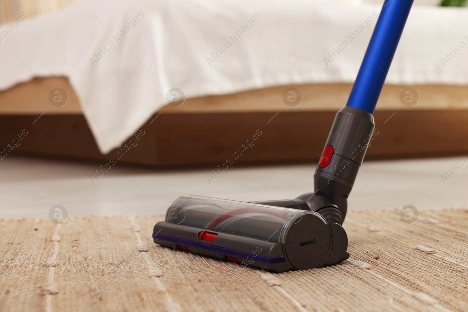 Photo of Cleaning rug with cordless vacuum cleaner indoors, closeup