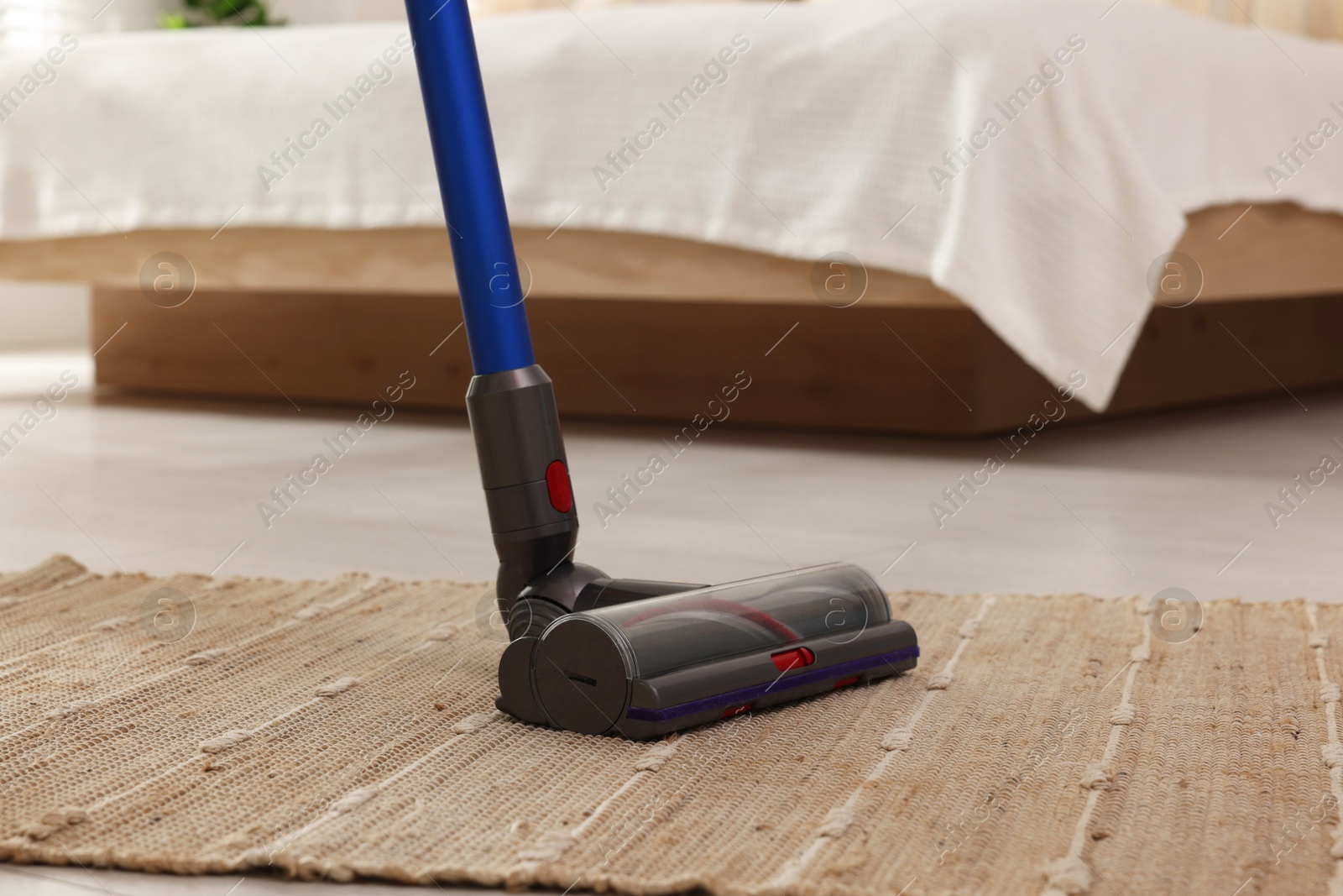 Photo of Cleaning rug with cordless vacuum cleaner indoors, closeup