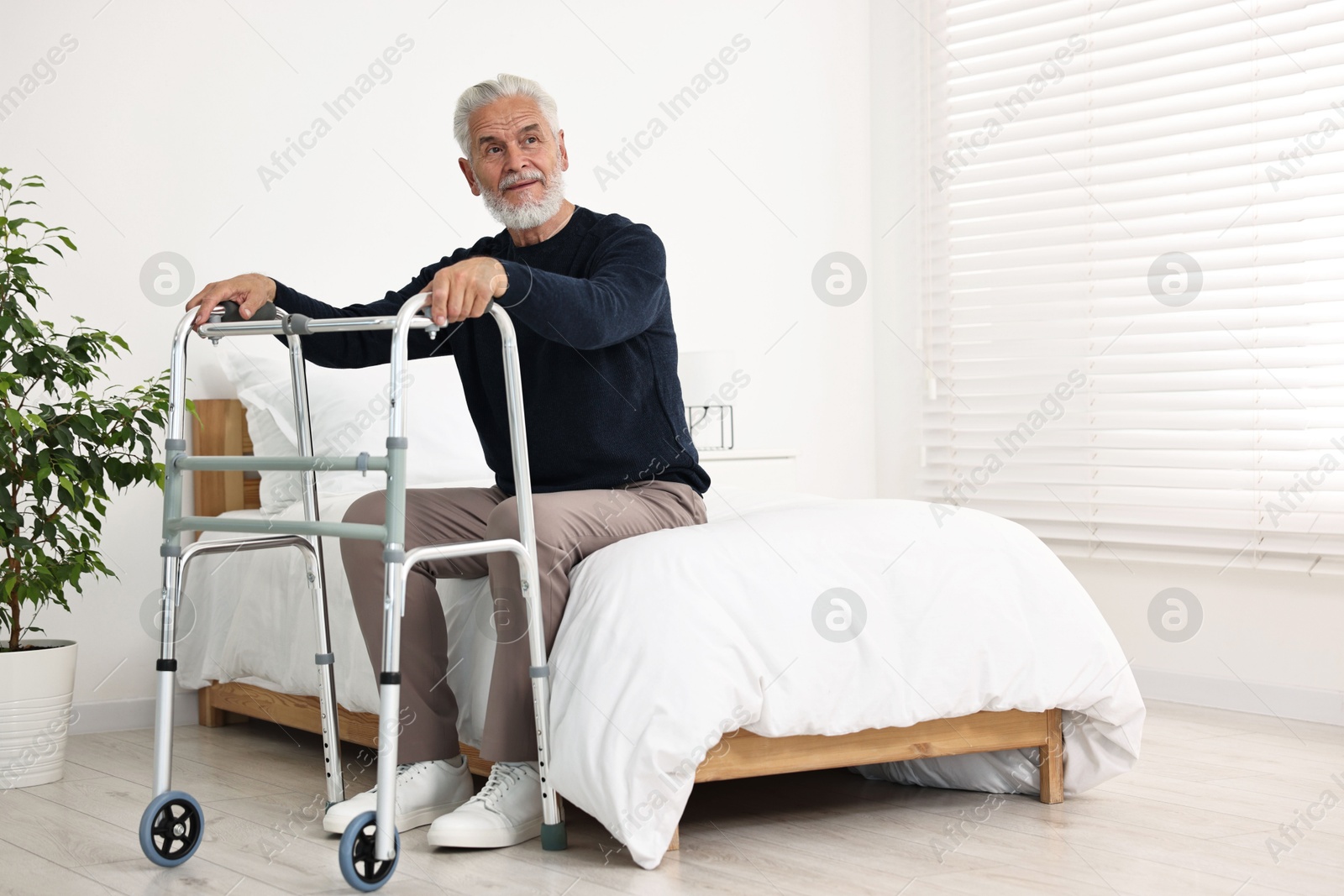 Photo of Senior man with walking frame on bed in hospital ward. Space for text