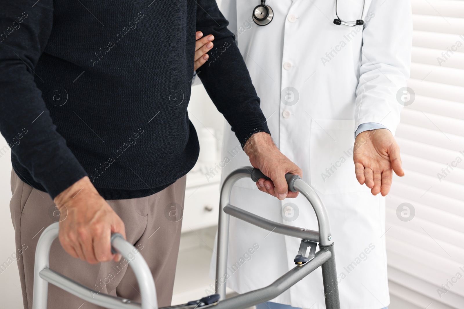 Photo of Doctor helping senior man with walking frame in clinic, closeup