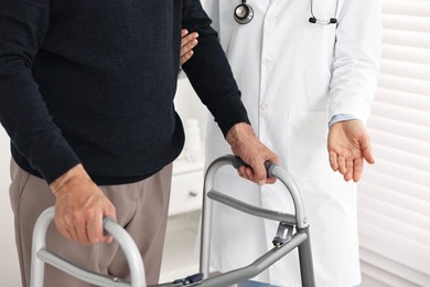 Photo of Doctor helping senior man with walking frame in clinic, closeup