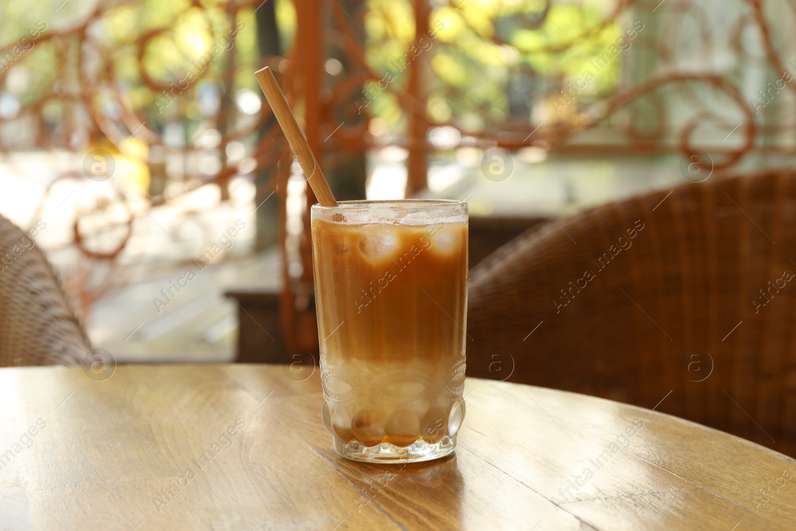 Photo of Glass of refreshing iced coffee and straw on wooden table outdoors