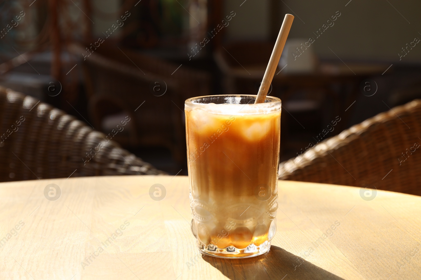 Photo of Glass of refreshing iced coffee and straw on wooden table outdoors