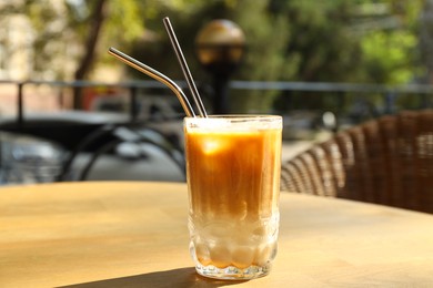 Photo of Glass of refreshing iced coffee and straws on wooden table outdoors