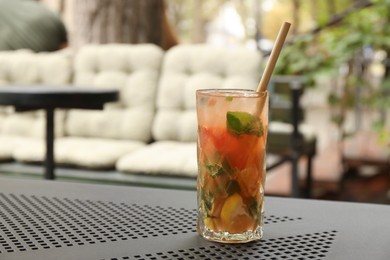 Photo of Glass of tasty refreshing drink and straw on table in outdoor cafe