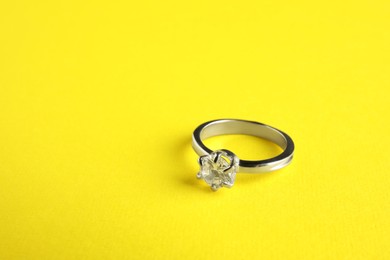 Photo of Beautiful bijouterie. Elegant ring on yellow background, closeup. Space for text