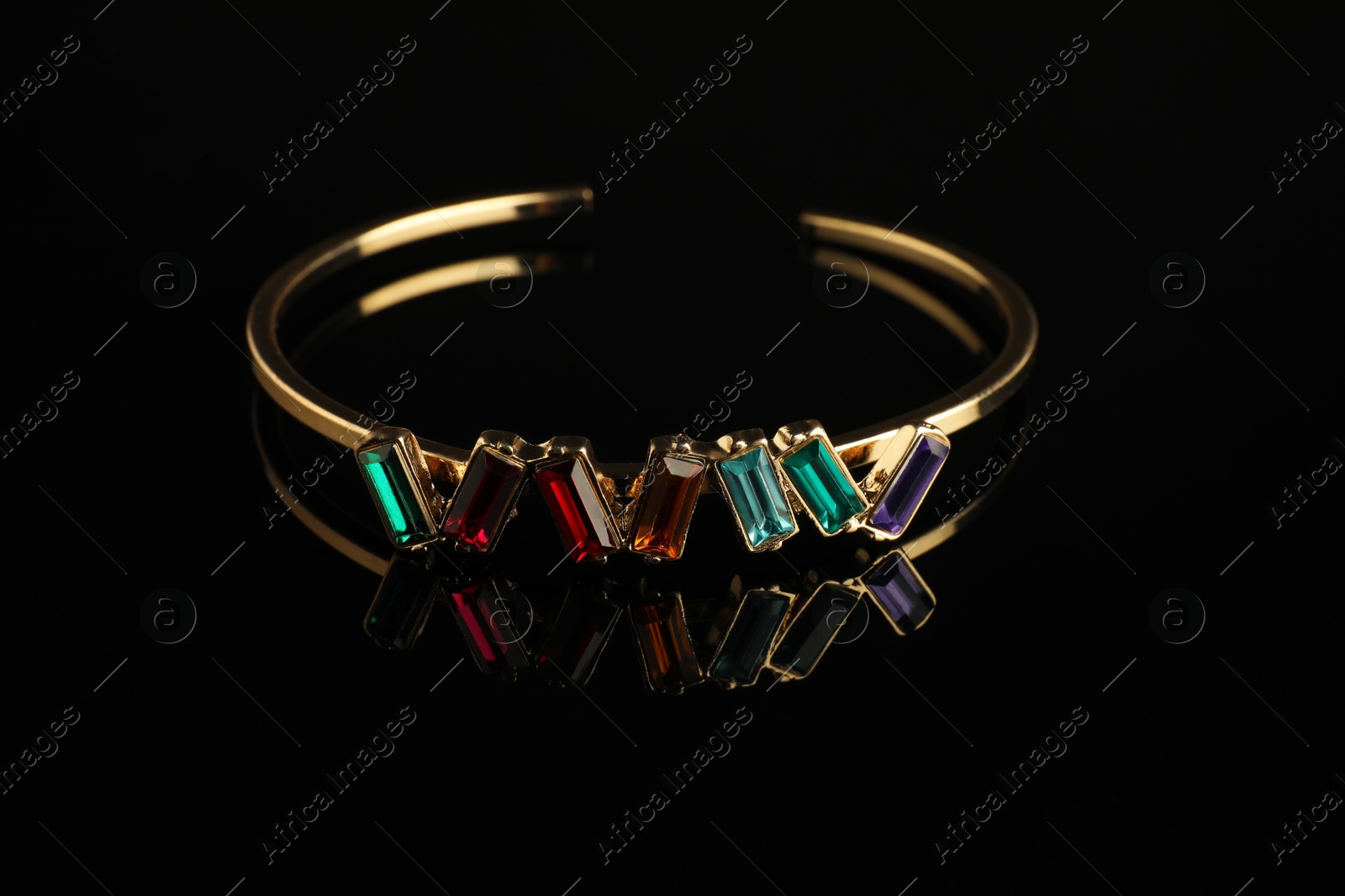 Photo of Beautiful bijouterie. Elegant bracelet on black mirror surface, closeup