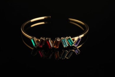 Photo of Beautiful bijouterie. Elegant bracelet on black mirror surface, closeup