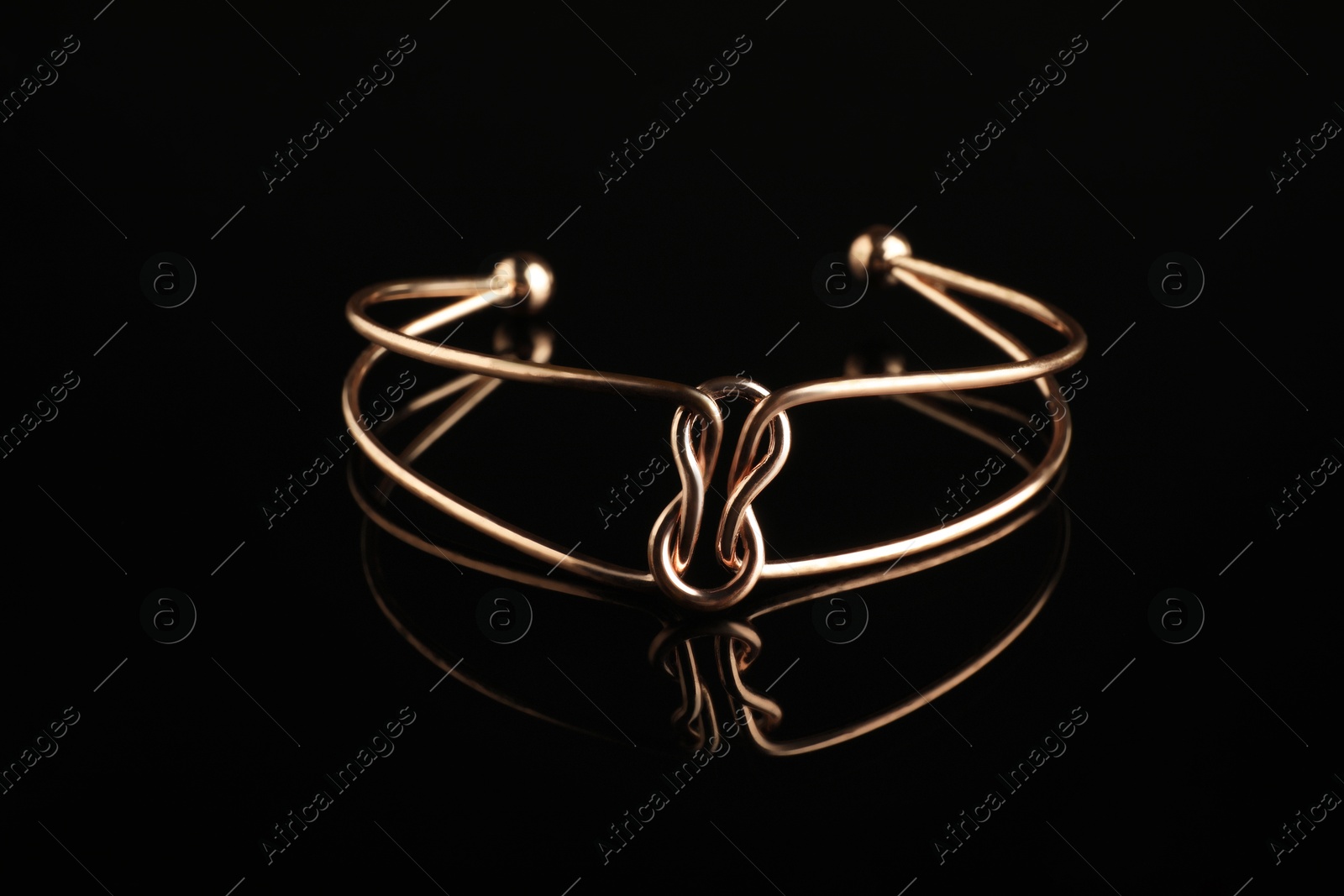 Photo of Beautiful bijouterie. Elegant bracelet on black mirror surface, closeup