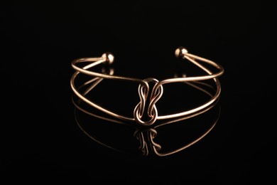 Photo of Beautiful bijouterie. Elegant bracelet on black mirror surface, closeup