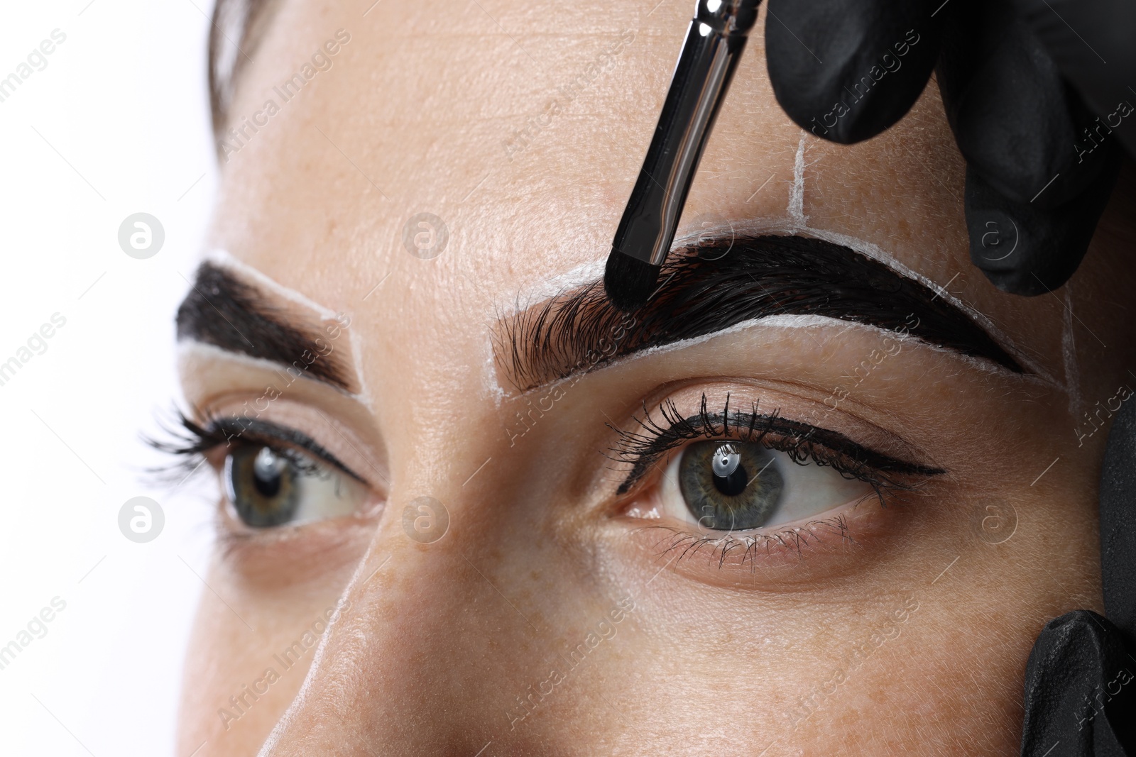 Photo of Young woman undergoing henna eyebrows dyeing on light background, closeup