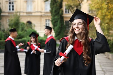 Photo of Happy students with diplomas after graduation ceremony outdoors, selective focus